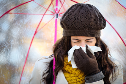 Mujer con gripe o resfriado tosiendo y sonándose la nariz con un papel bajo una lluvia de otoño